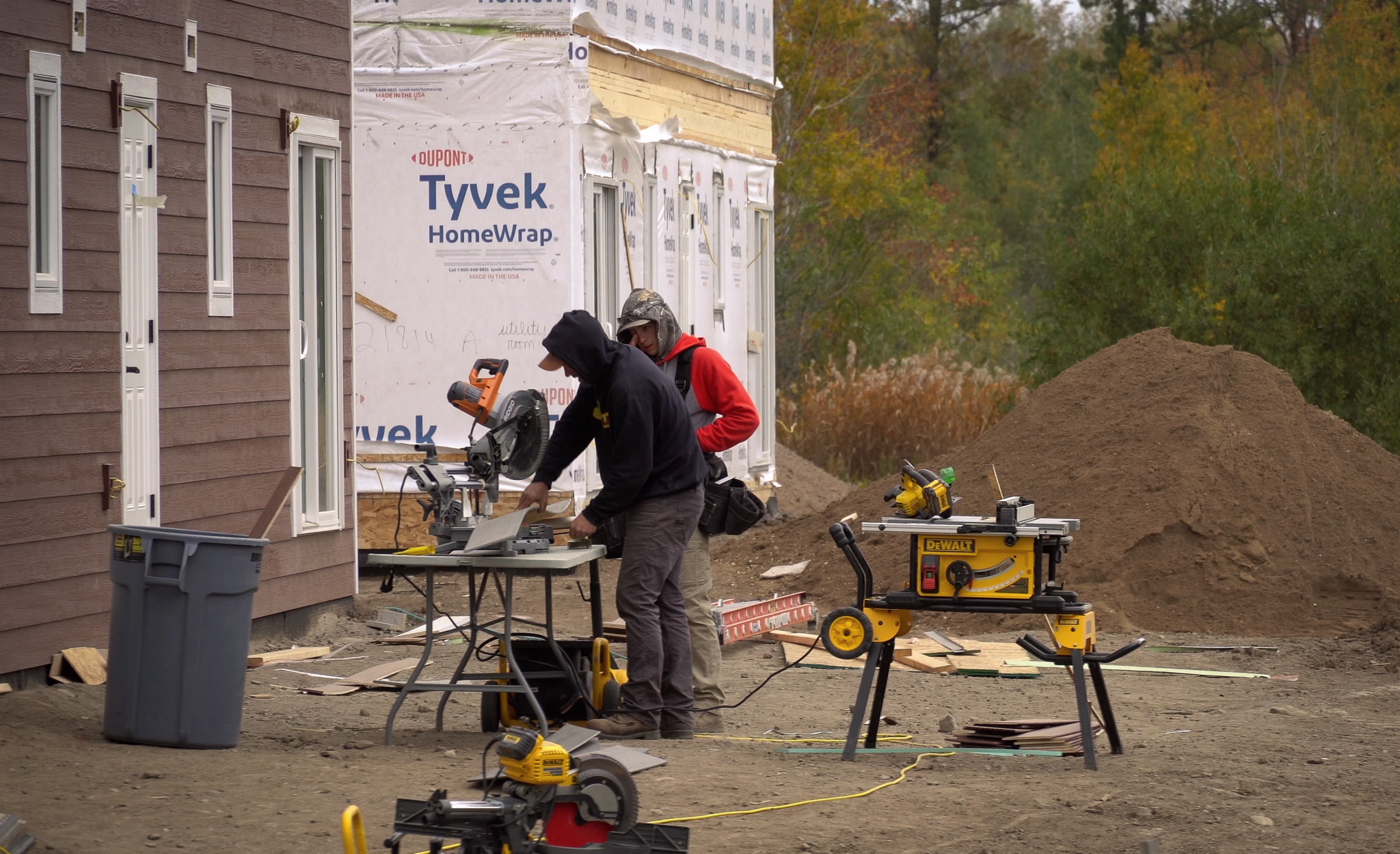 Construction male workers using a saw in front of under construction homes 