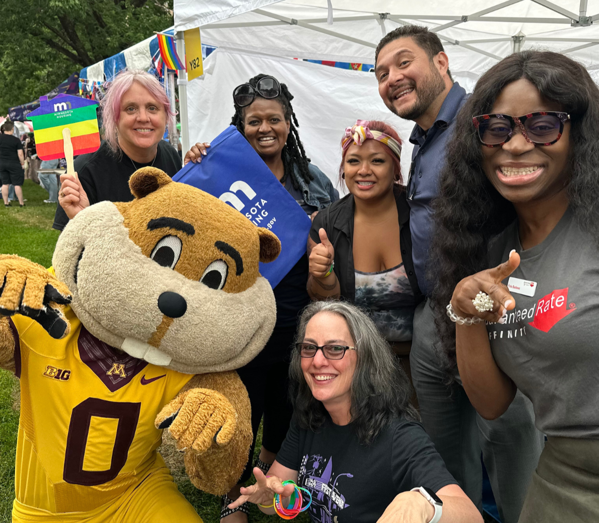 Staff and mascot smiling and pointing at camera