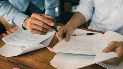 Close-up of two people sitting at a desk reviewing multi-page documents.