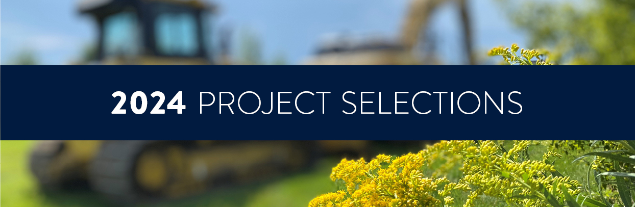 Backhoe on grass with yellow flower and text: "2024 Project Selections"