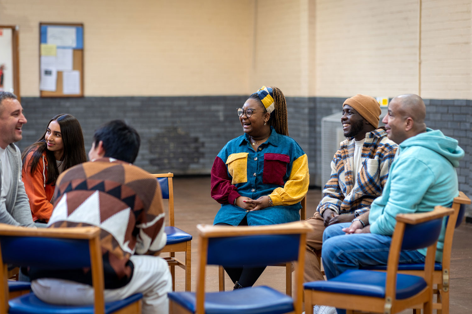 Diverse group of participants laughing and engaging while sitting in a circle of chairs in a large community setting.